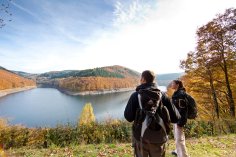 Wanderer blicken auf die herbstliche Riveris Talsperre